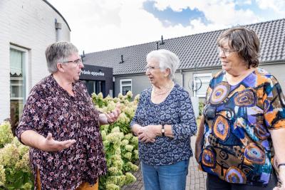 Drie dames overleggen voor de ingang van een huis van de wijk