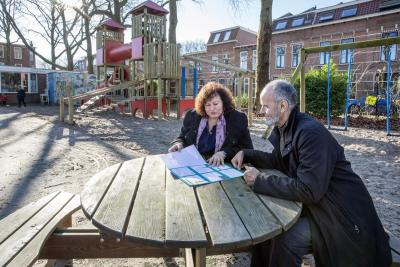 Een medewerker en een inwoner bekijken buiten aan een tafel een folder